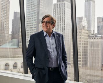 A man in glasses standing at a window.