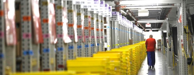A worker transports plastic crates filled with orders at a distribution center.
